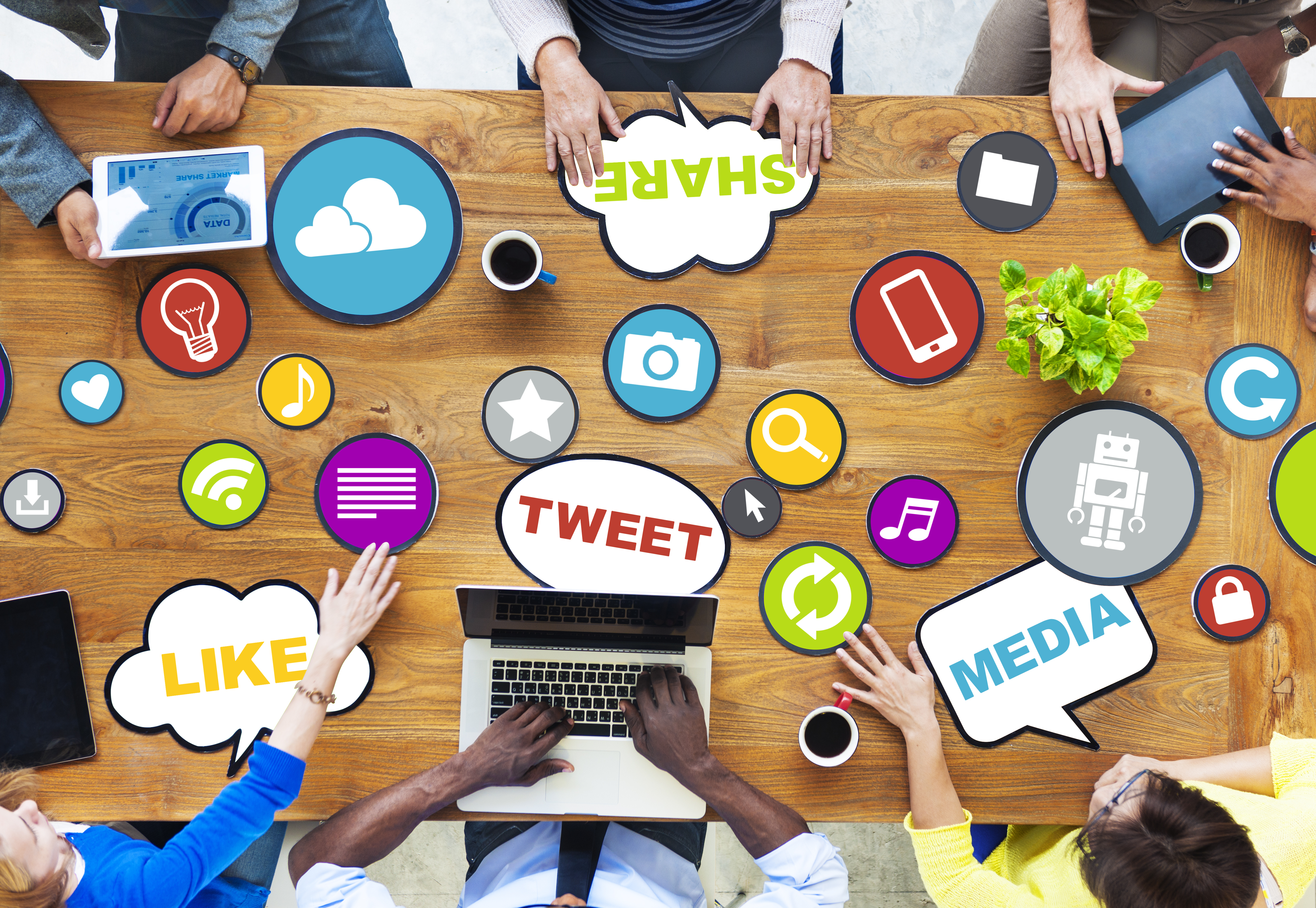 Six people work around a table with various phrases and icons overlaid in their
                workspace such as MEDIA, TWEET, LIKE, SHARE and icons representing images, music, mobile phones, ideas and post reactions